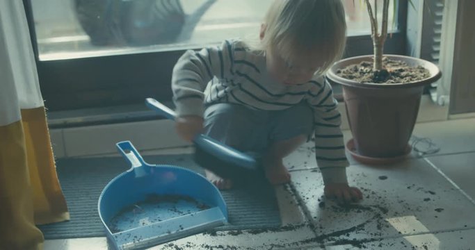Little toddler using dustpan and brush at home