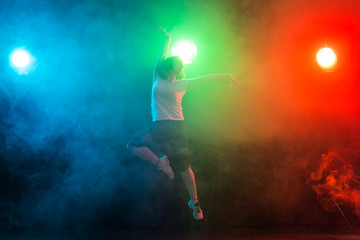 Fototapeta na wymiar Cheerleading young woman dancing on colourful dark background