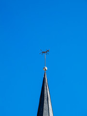 Weather vane in the shape of a donkey on the spire of the old Church of St. Lawrence in Diekirch, Luxembourg against a clear blue sky