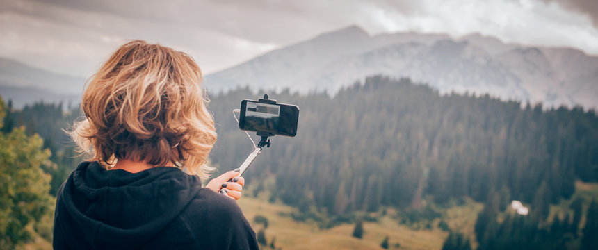 Woman taking selfie picture on landscape background using photo stick