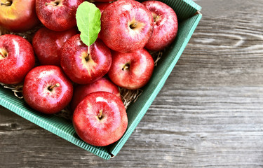 A lot of fresh Royal Red Gala apples and green leaf in paper box on wooden background.