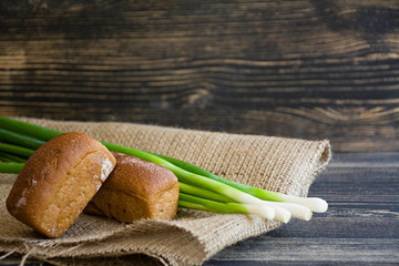 Freshly baked bread and green onion on a dark wooden background.