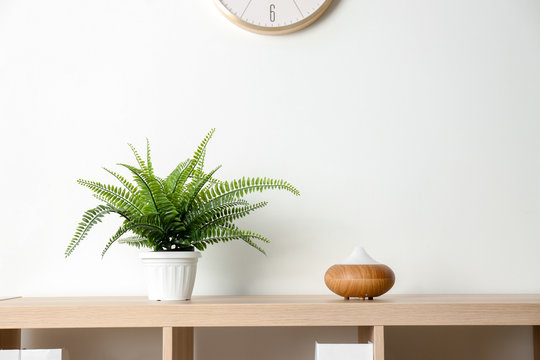 Modern aroma lamp and houseplant on wooden shelf near light wall