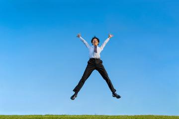 Fototapeta na wymiar 青空をバックにバンザイしながらジャンプするスーツ姿の若いビジネスマン1人。成功・達成・成就・元気・健康イメージ
