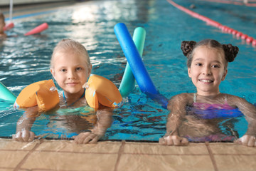 Little girls with swimming noodles in indoor pool