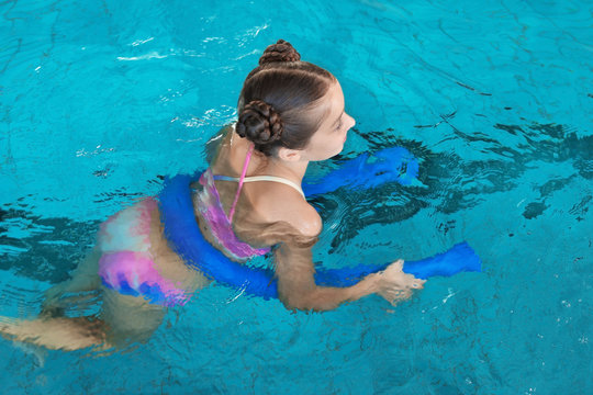 Little girl with swimming noodle in indoor pool