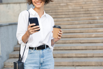 Amazing woman on the street using mobile phone holding coffee.