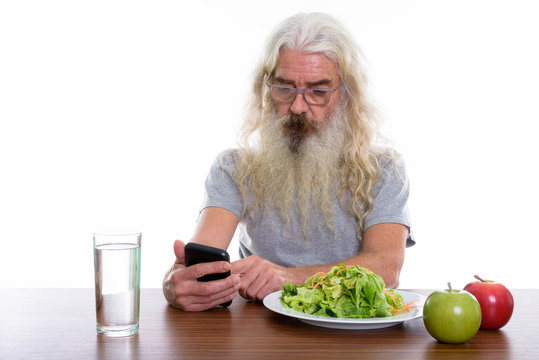 Studio shot of senior bearded man using mobile phone with health