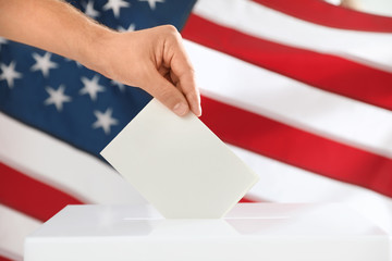 Man putting ballot paper into box and American flag on background, closeup