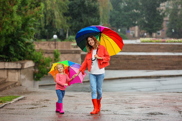 Happy mother and daughter with bright umbrella under rain outdoors