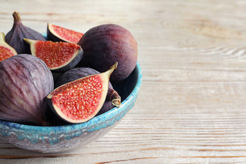 Bowl with fresh ripe figs on wooden background. Space for text