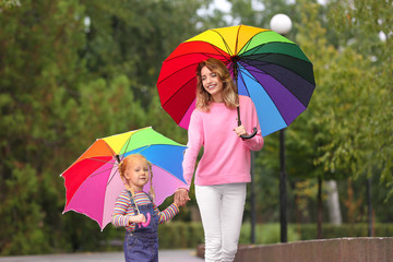 Happy mother and daughter with bright umbrellas walking in park