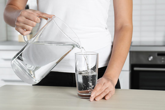Woman pouring water into glass at table, closeup