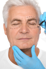 Doctor marking senior man face before cosmetic surgery on white background