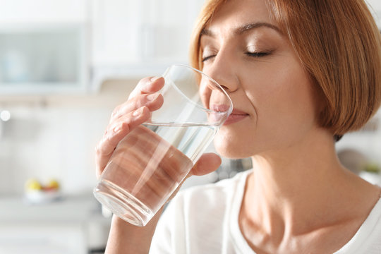 Woman drinking clean water from glass in kitchen, closeup