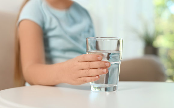 Cute little girl holding glass of fresh water indoors, closeup
