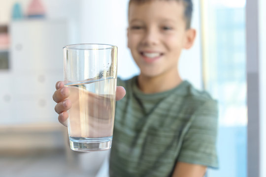 Little boy holding glass of fresh water indoors