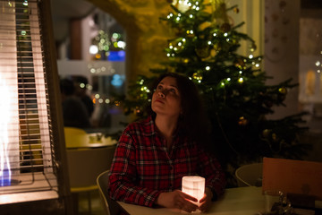Holiday, Christmas and people concept - Young woman sitting in cafe near Christmas tree background at night