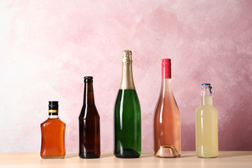 Bottles with different alcoholic drinks on table against color background