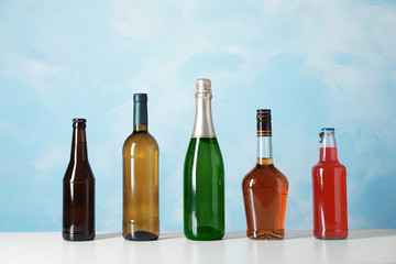 Bottles with different alcoholic drinks on table against color background