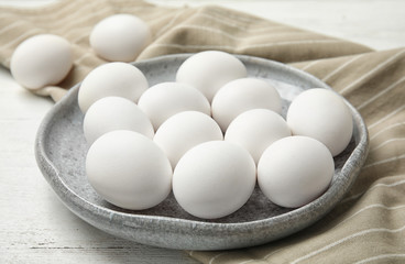 Plate with raw chicken eggs on wooden table