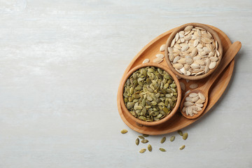 Raw pumpkin seeds in dish on light background, top view. Space for text