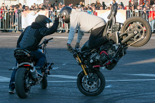 Two bikers perform motorcycle stunt riding Stoppie (Endo) trick