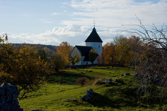 Viking burrial feld with church from 1200s in Adels&ouml; at lake M&auml;laren, Stockholm, a  pale autumn day with blue sky and sea with  clouds and orange leafs
