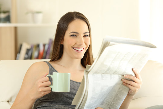 Woman holding newspaper and coffee cup looking at camera