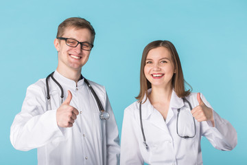 Two best smart professional smiling doctors workers in white coats showing thumbs up standing against blue background