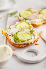 Breakfast cream cheese, cucumber and radish sandwiches on a wooden board.