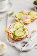 Breakfast cream cheese, cucumber and radish sandwiches on a wooden board.
