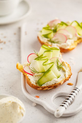 Breakfast cream cheese, cucumber and radish sandwiches on a white board.