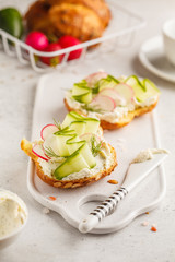 Breakfast cream cheese, cucumber and radish sandwiches on a white board.