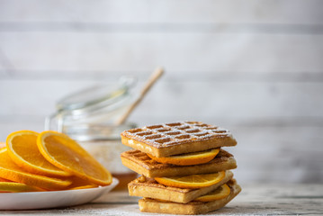 Tasty waffles with sliced oranges on light wooden table. Close up, Selective focus