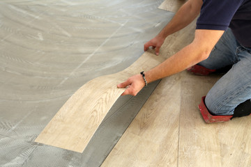 Work on laying flooring. Worker installing new vinyl tile floor.