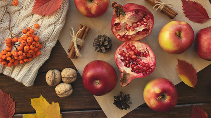 Apples, pomegranate, cinnamon, cones, walnuts, fallen leaves on a wooden background. Autumn composition.