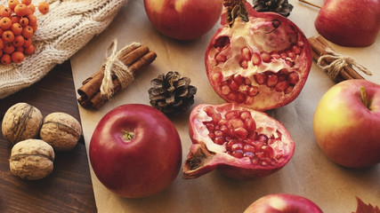 Apples, pomegranate, cinnamon, cones, walnuts, fallen leaves on a wooden background. Autumn composition.