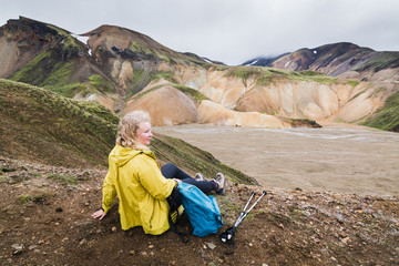 Fototapeta premium Woman in yellow raincoat overlooking the colourful mountains in Landmannalaugar national park, Iceland