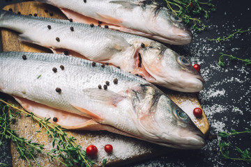 Fresh raw sea bass fish with spices, salt, lemon and thyme on a wooden kitchen board before cooking. Sea bass fish