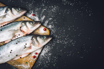 Fresh raw sea bass fish with spices, salt, lemon and thyme on a wooden kitchen board before cooking. Sea bass fish. Copy space.