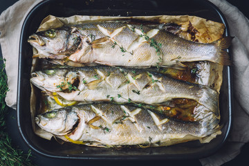 Baked (or fried grilled) sea bass fish with spices, salt, lemon and thyme on a wooden board before...