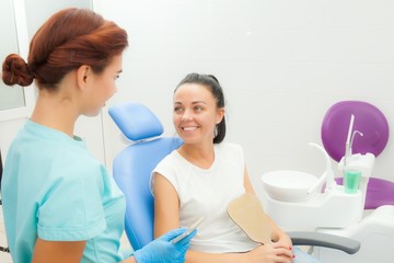 Fototapeta premium Beautiful female patient with dental treatment in the dentist office. A woman visiting her dentist. Women look at each other