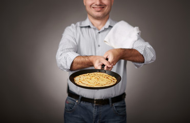 man posing with a pancake in a pan, white shirt and pants, gray background, shallow depth of field, sharp pancake and blurred face