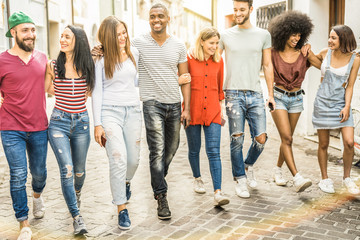 Fototapeta premium Multiracial millennial friends walking and talking in city center - Happy guys and girls having fun around old town streets - University students on travel vacations - Warm shadow filter tone