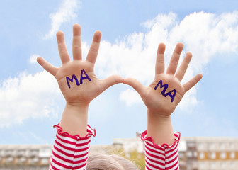 The child's hand on a background of blue sky with written in marker on the palms of the word mother in Russian.
