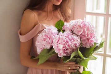 Beautiful woman holding a pink hydrangeas in her arms. 