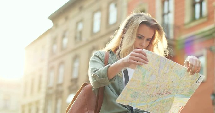 Caucasian young pretty woman in casual style standing in the town with a map in hands and looking for the route.