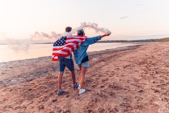 american couple walking along the beach and holding hand flare or fusee covered in american flag. Freedom and independence concept