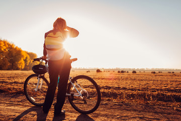 Middle-aged woman bicyclist riding in autumn field at sunset. Senior sportswoman admiring the view.